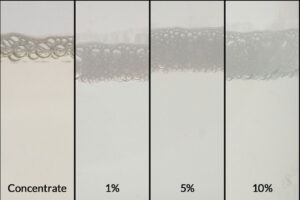 Imagen del concentrado de producto ZERUST AxxaWash KMS-305AL junto con sus diluciones al 1 %, 5 % y 10 %, diseñado para una limpieza eficiente de piezas de aluminio.