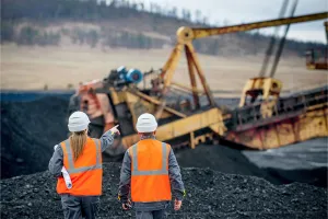 Empleados de una mina en un sitio con equipo oxidado al fondo, mostrando el impacto de la corrosiÃ³n en el equipo minero.