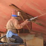 Trabajador realizando granallado húmedo en la pared de un tanque antes de pintar.